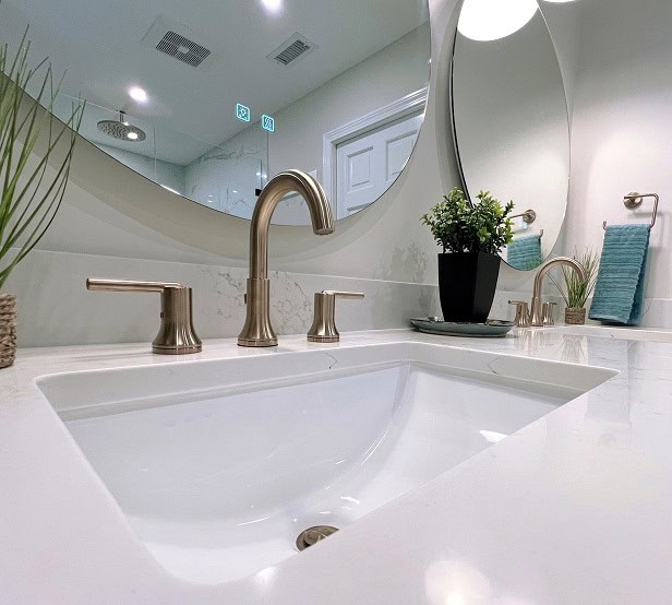 Sleek double vanity with brushed gold fixtures and curved mirror – contemporary bathroom renovation in historic home in Beverly, Massachusetts